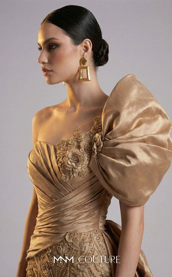 MNM Couture F03065 champagne gold satin mermaid gown with oversized left-shoulder bow, 3D gold rose appliqués, ruched asymmetric sweetheart bodice, gold corded lace skirt, and sweeping side overskirt | Couture Shop LA.