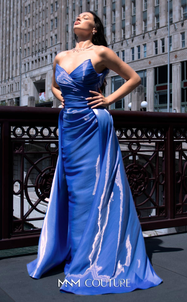 A glamorous MNM Couture G1419 metallic sheath gown featuring a strapless pleated bodice, faux-wrap design, pointed neckline, and a dramatic overskirt. | Couture Shop LA