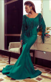 An elegant MNM Couture 2340 mermaid gown with a plunging neckline, sheer inset, fringe-detailed cutaway sleeves, and a sweep train, offering haute couture sophistication.