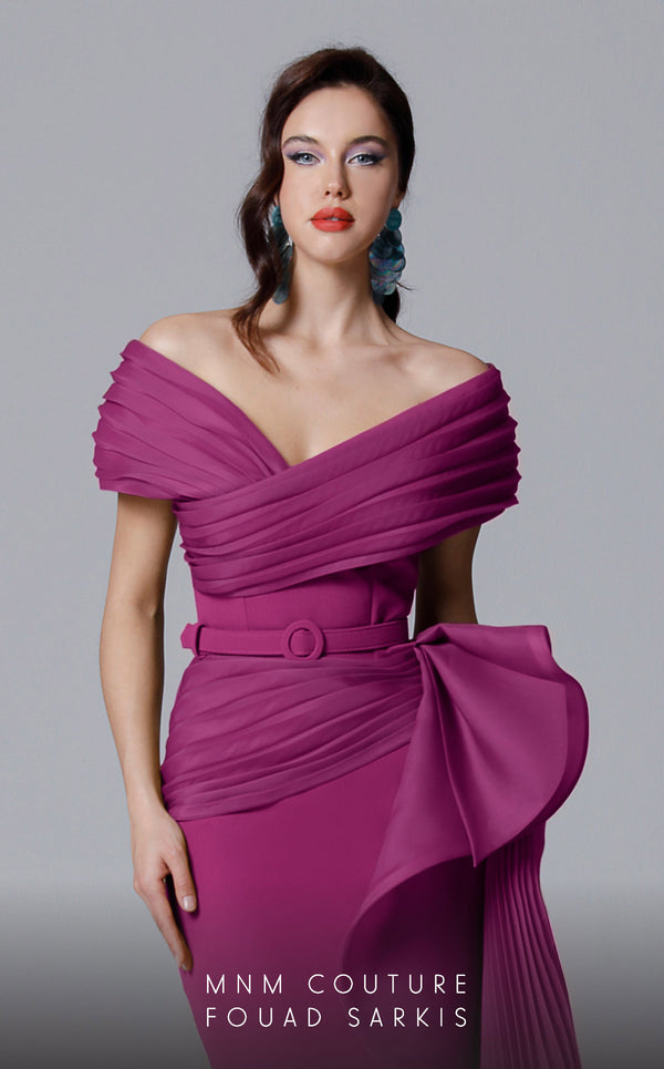 A sophisticated MNM Couture 2692 off-shoulder mermaid gown featuring pleated foldover details, ruffled side peplums, and a sweeping train. | Couture Shop LA