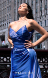 A glamorous MNM Couture G1419 metallic sheath gown featuring a strapless pleated bodice, faux-wrap design, pointed neckline, and a dramatic overskirt. | Couture Shop LA