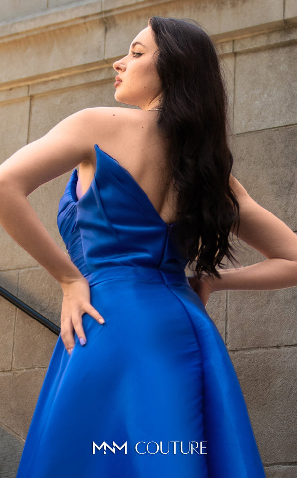 A glamorous MNM Couture G1419 metallic sheath gown featuring a strapless pleated bodice, faux-wrap design, pointed neckline, and a dramatic overskirt. | Couture Shop LA