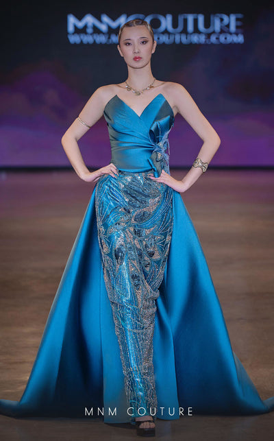 MNM Couture Style J03497 strapless column gown with a beaded skirt, satin train, and asymmetrical deep V-neck. \ Couture Shop LA