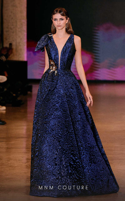 MNM Couture Style Q1150 navy blue brocade ballgown with deep V-neckline, mesh inset, bow detail, and gold and crystal floral embellishments at waist and shoulder. | Couture Shop LA