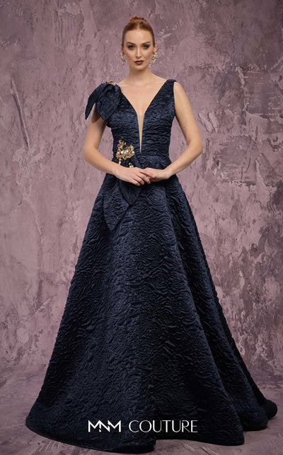 MNM Couture Style Q1150 navy blue brocade ballgown with deep V-neckline, mesh inset, bow detail, and gold and crystal floral embellishments at waist and shoulder. | Couture Shop LA
