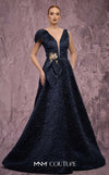 MNM Couture Style Q1150 navy blue brocade ballgown with deep V-neckline, mesh inset, bow detail, and gold and crystal floral embellishments at waist and shoulder. | Couture Shop LA