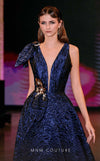 MNM Couture Style Q1150 navy blue brocade ballgown with deep V-neckline, mesh inset, bow detail, and gold and crystal floral embellishments at waist and shoulder. | Couture Shop LA
