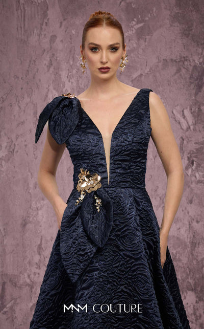 MNM Couture Style Q1150 navy blue brocade ballgown with deep V-neckline, mesh inset, bow detail, and gold and crystal floral embellishments at waist and shoulder. | Couture Shop LA